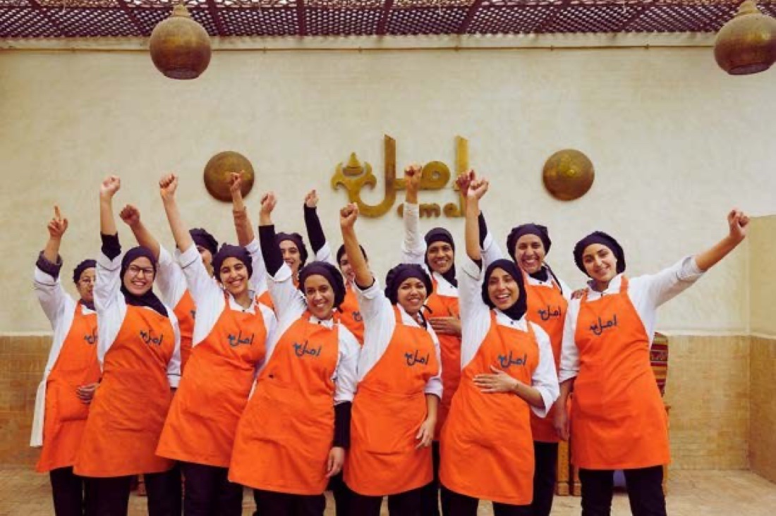 Amal women in aprons celebrating together, arms raised